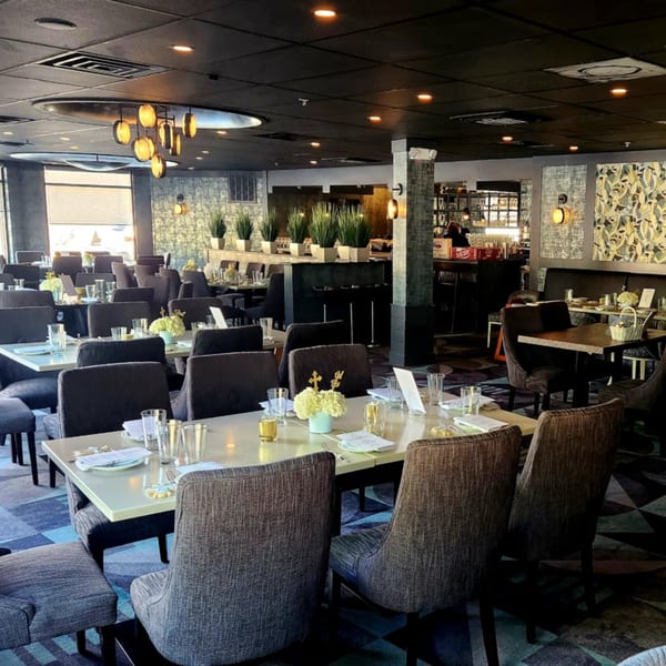 Jessica's Restaurant dining room with set tables, modern chandeliers, and a bar area in the background.