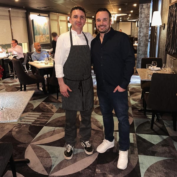 Jessica's Restaurant chef in a striped apron with a man in a dark shirt, standing in the dining room.