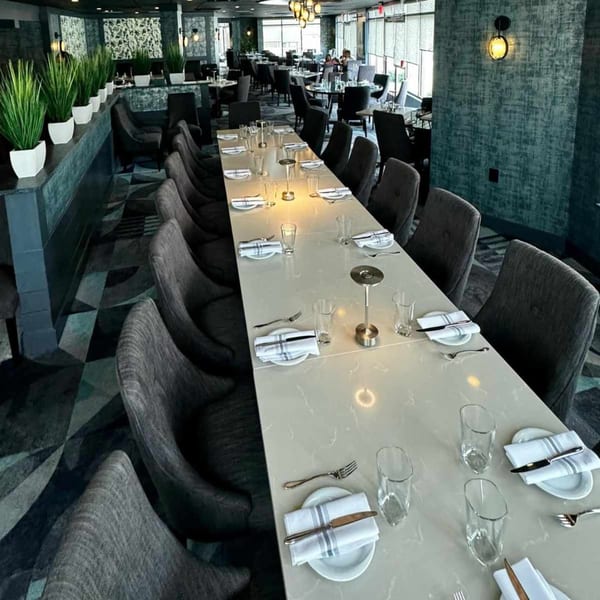 Long dining table set for many guests in a modern Italian restaurant with dark decor.