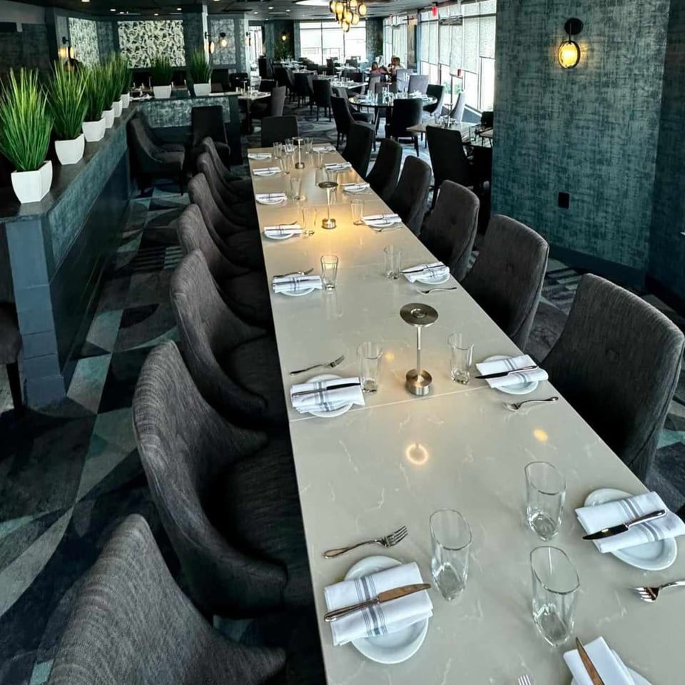 Long dining table set for many guests in a modern Italian restaurant with dark decor.