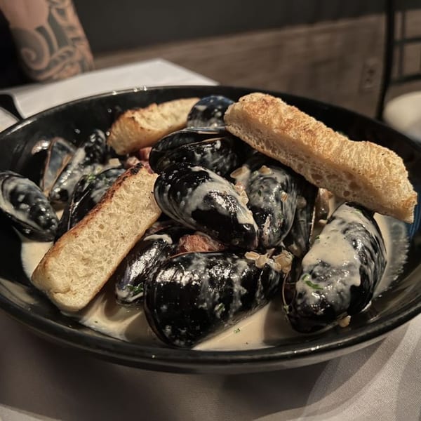 A black bowl of mussels in a creamy sauce with toasted bread at Jessica's Restaurant.
