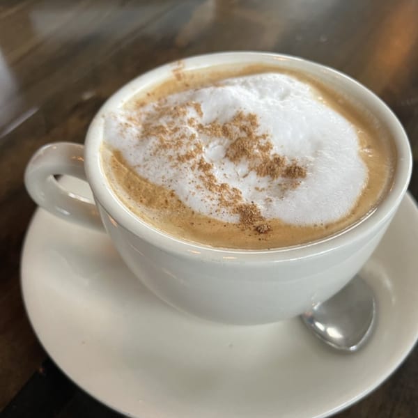 A white cup of Jessica's Restaurant Italian cappuccino with frothy milk and cinnamon on a saucer.