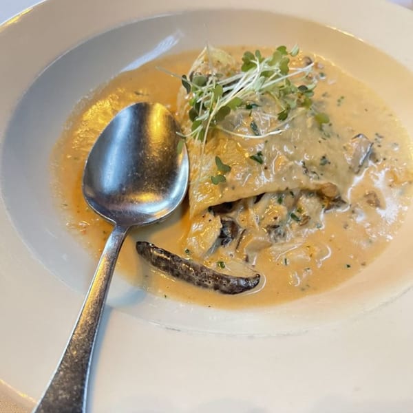 Italian pasta dish with creamy sauce, mushrooms, and microgreens in a white bowl with a spoon.