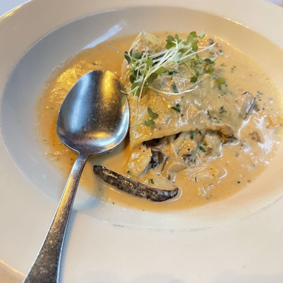 Italian pasta dish with creamy sauce, mushrooms, and microgreens in a white bowl with a spoon.