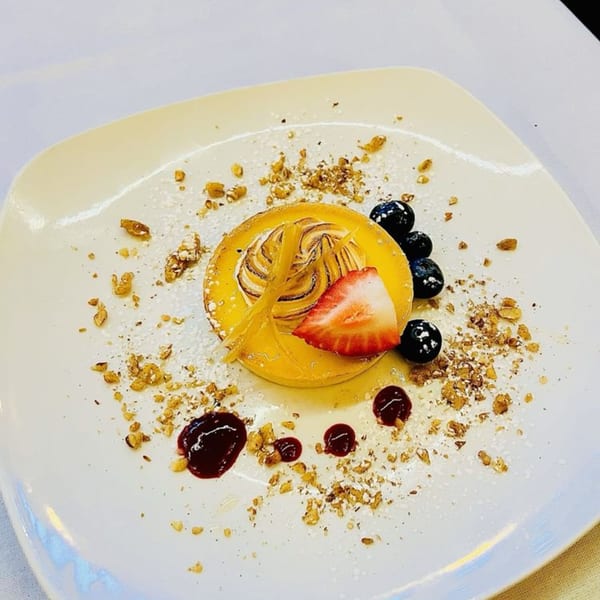 A lemon tart with meringue, fresh blueberries, a strawberry slice, and candied lemon peel.